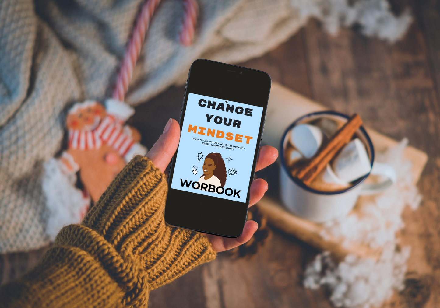 Hand holding a phone with 'Change Your Mindset Workbook' app on a cozy background