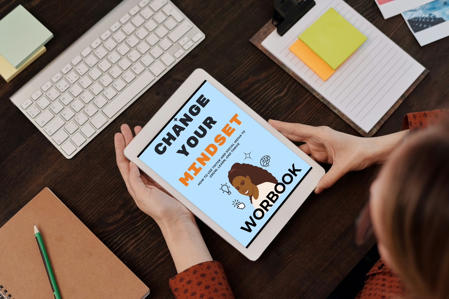 Person holding a tablet with 'Change Your Mindset Workbook' on a desk with stationery items.